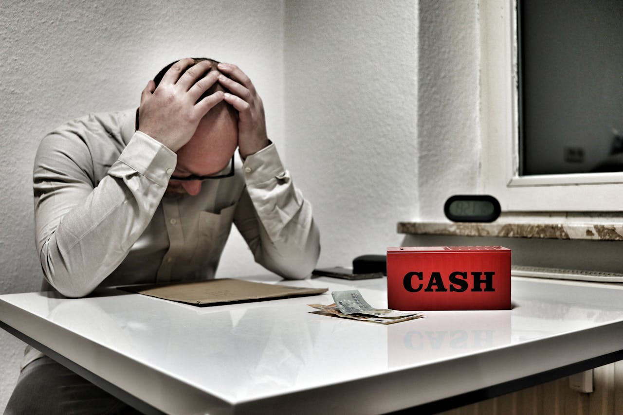 Persona muy preocupada sobre escritorio, con una caja de cash roja frente a él y un folder, reflexionando sobre la estrategia correcta para su fondo de emergencias