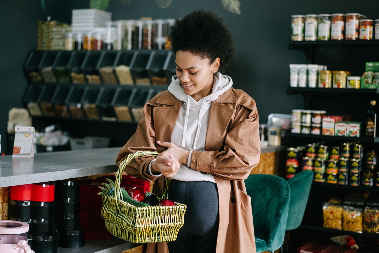 Persona con cesta de compras, viendo su plan de gastos en el celular, tomando una decisión de compra consciente y deliberada, con metas financieras claras, ilustrando el concepto de gasto consciente.