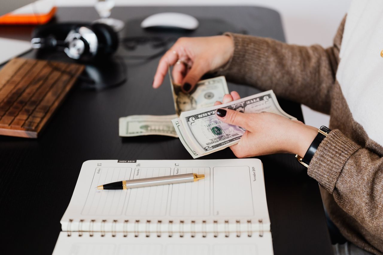 Persona con cuaderno y dinero organizándose para encontrar la mejor forma de gastar