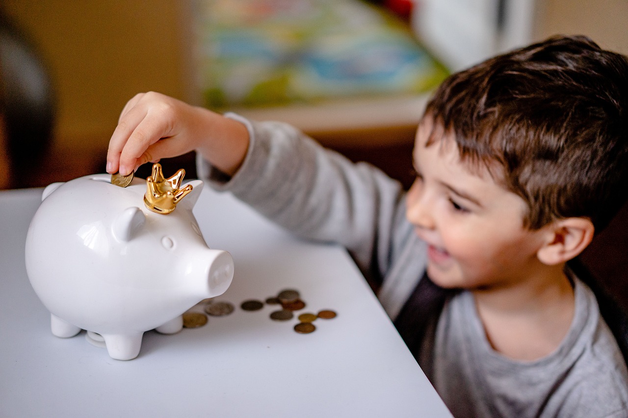 Niño guardando monedas en una alcancía de barro, hábito de ahorro desde temprana edad