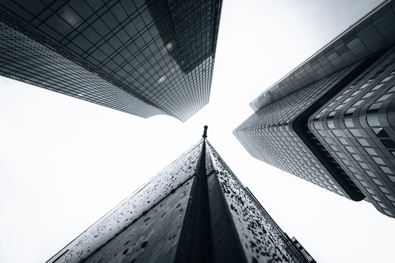 Vista desde abajo de tres edificios corporativos que convergen hacia el cielo, como metáfora de comparar opciones al elegir una casa de bolsa para invertir