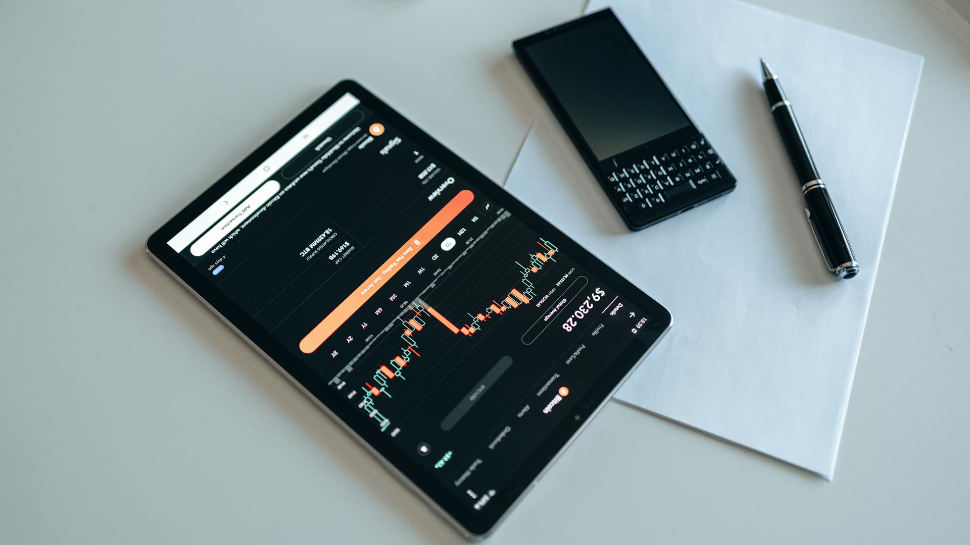 Pantalla de tablet con gráfica de inversiones y celular sobre papel describiendo forma activa o pasiva de invertir