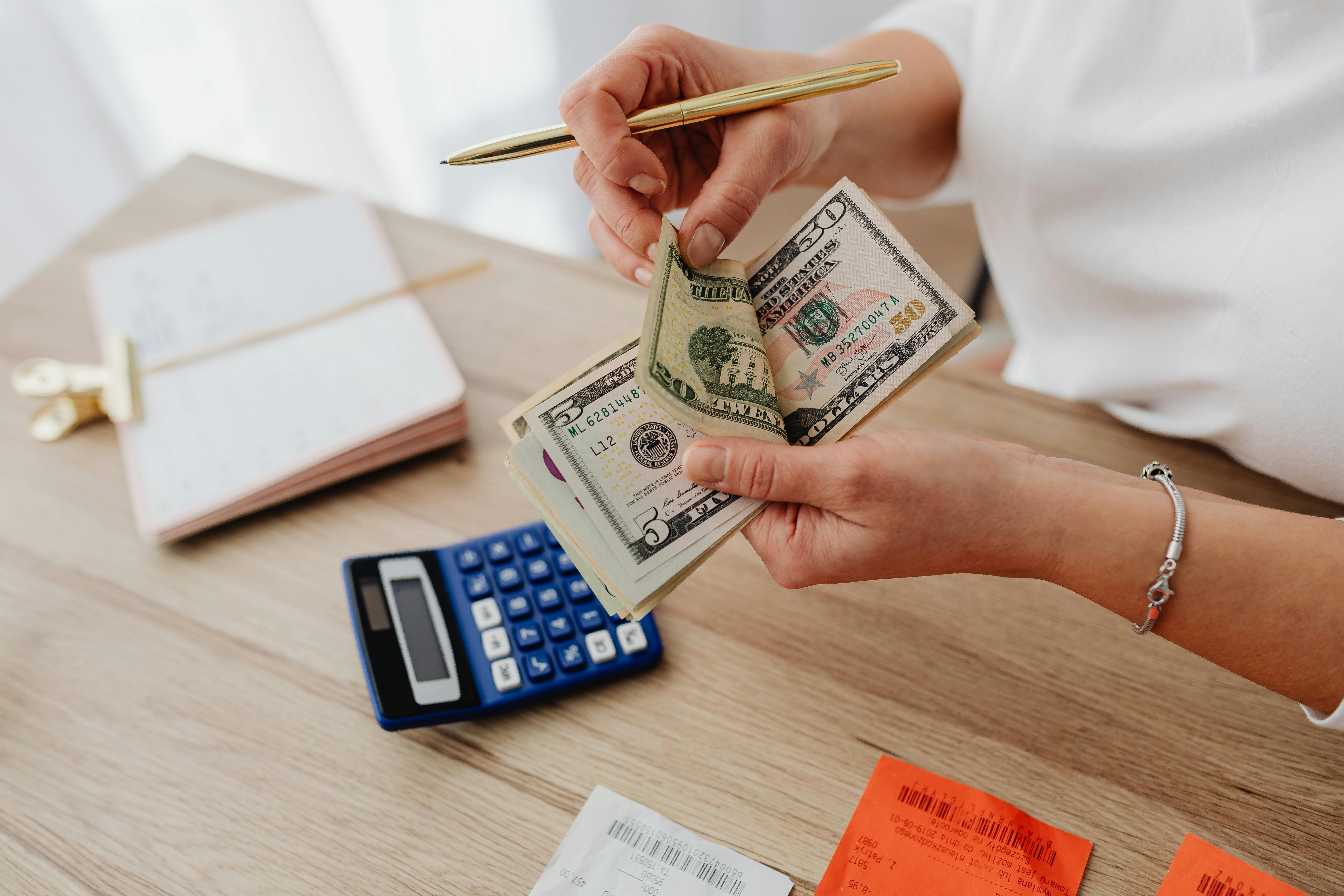 Persona con calculadora, billetes y anotando gastos, claramente haciendo su plan de gastos usando el método YNAB