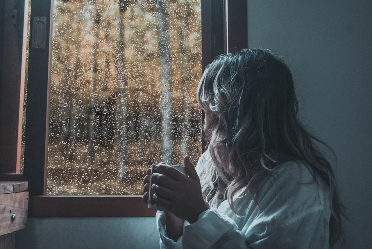 Persona en casa mirando la lluvia por la ventana con tranquilidad, representando la seguridad de tener un fondo para emergencias completo